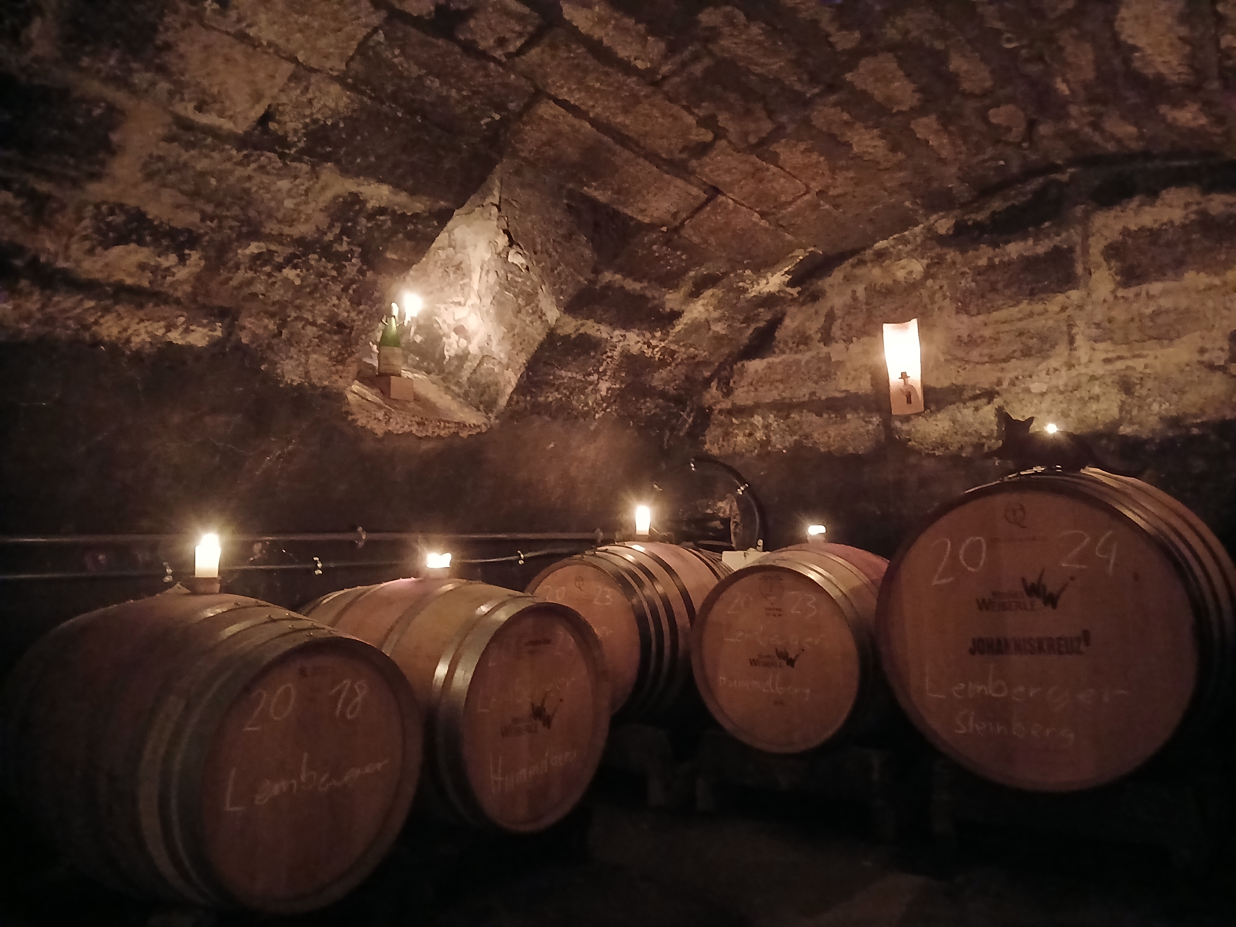 Ein stimmungsvoller Weinkeller mit mehreren Holzfässern, die von Kerzenlicht erleuchtet werden.